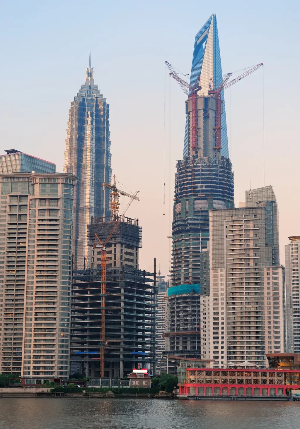 Supertall skyscraper under construction with tower cranes beside a riverfront skyline