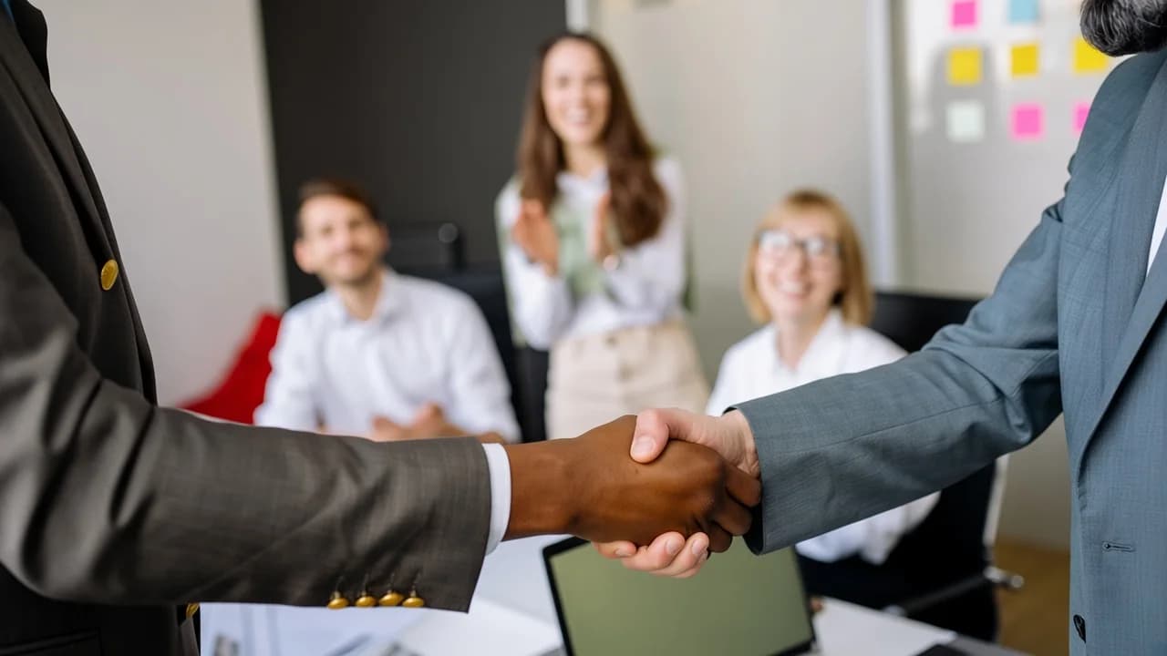 Business handshake in an office while colleagues applaud in the background